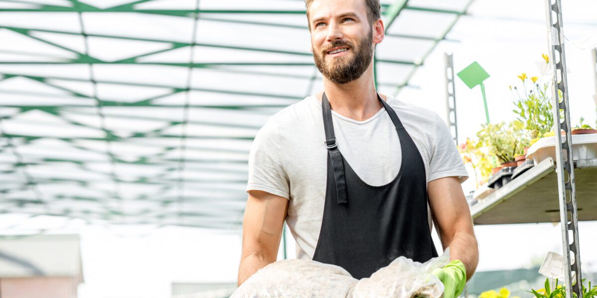 Handsome,Gardener,With,Apron,And,Working,Gloves,Carrying,Bag,With