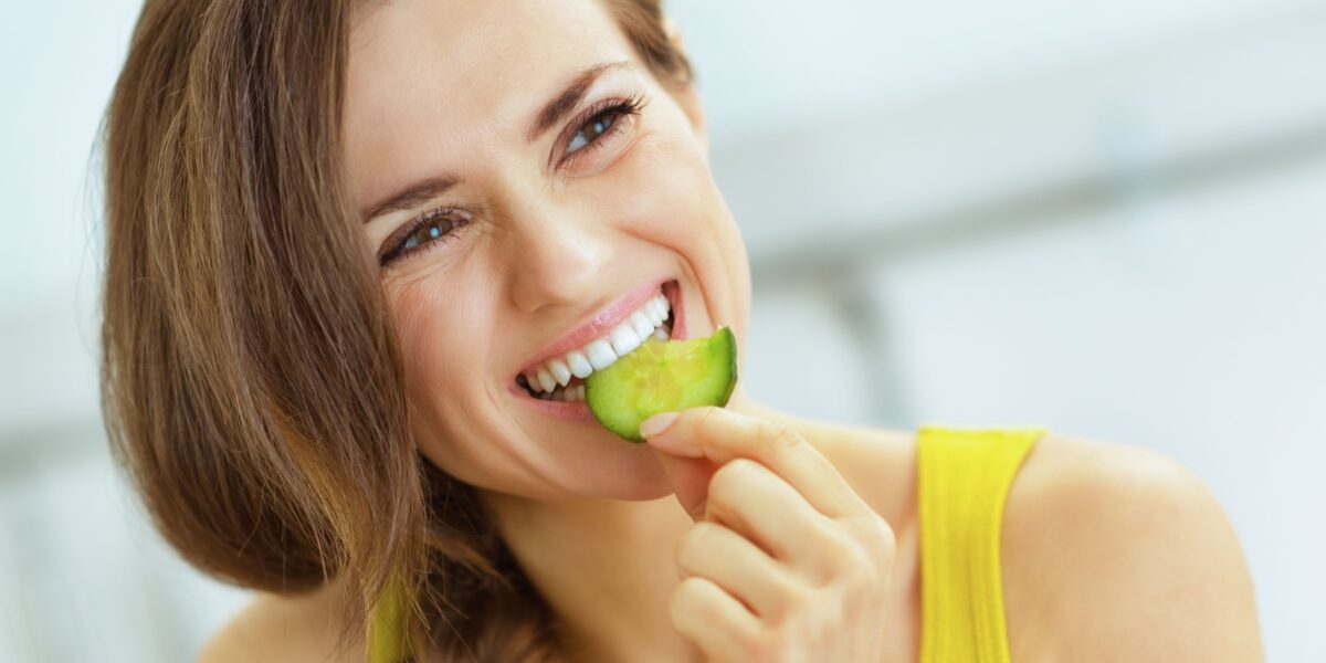 Young,Woman,Eating,Cucumber,In,Kitchen