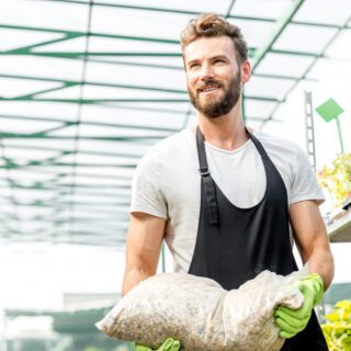 Handsome,Gardener,With,Apron,And,Working,Gloves,Carrying,Bag,With