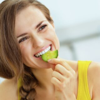 Young,Woman,Eating,Cucumber,In,Kitchen