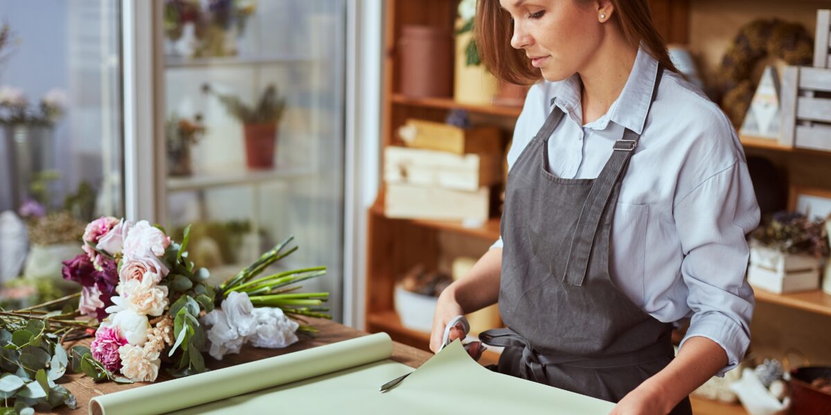 Close,Up,Of,Female,Florist,Hands,Cutting,Color,Wrapping,Paper